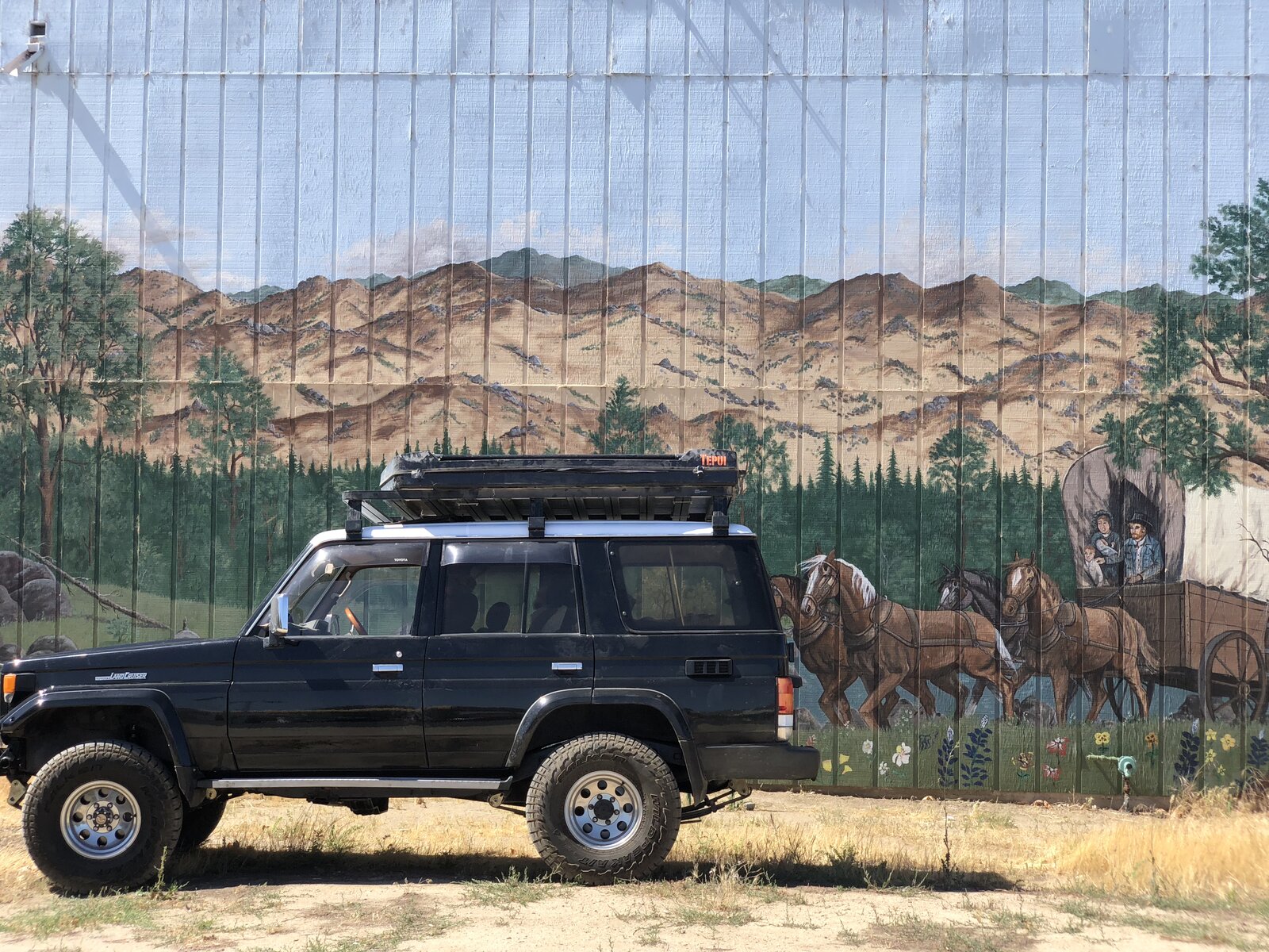70 Series Land Cruiser with rooftop tent in front of a wagon train mural
