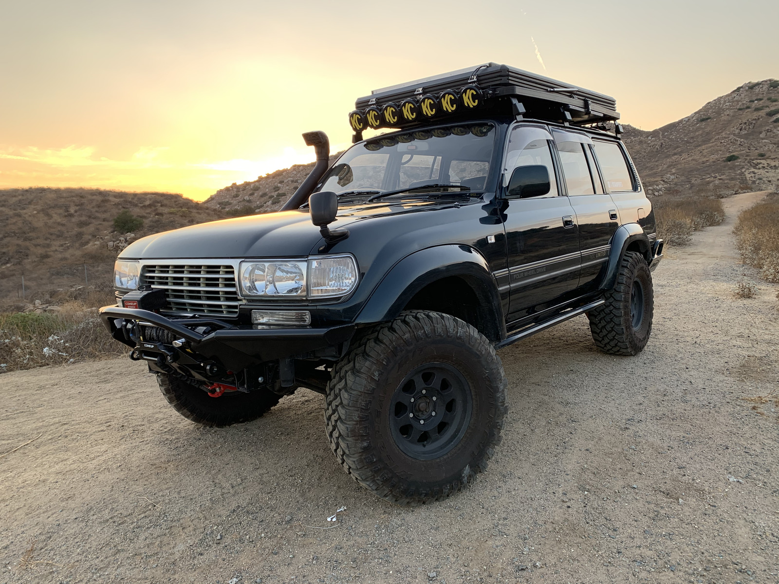 80 Series Land Cruiser with roof top tent and light bar at sunset