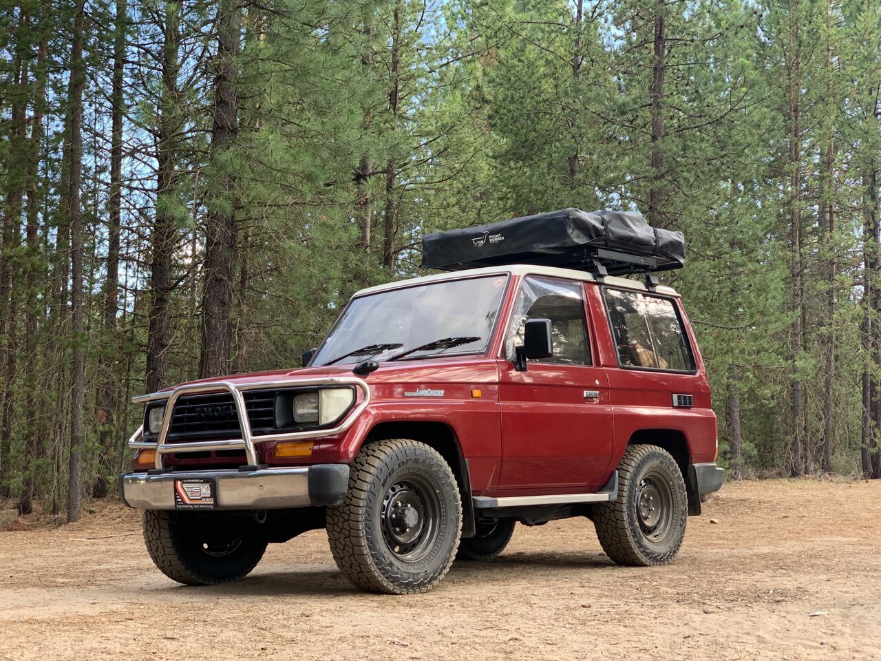 Red Prado Land Cruiser with rooftop tent in the forest