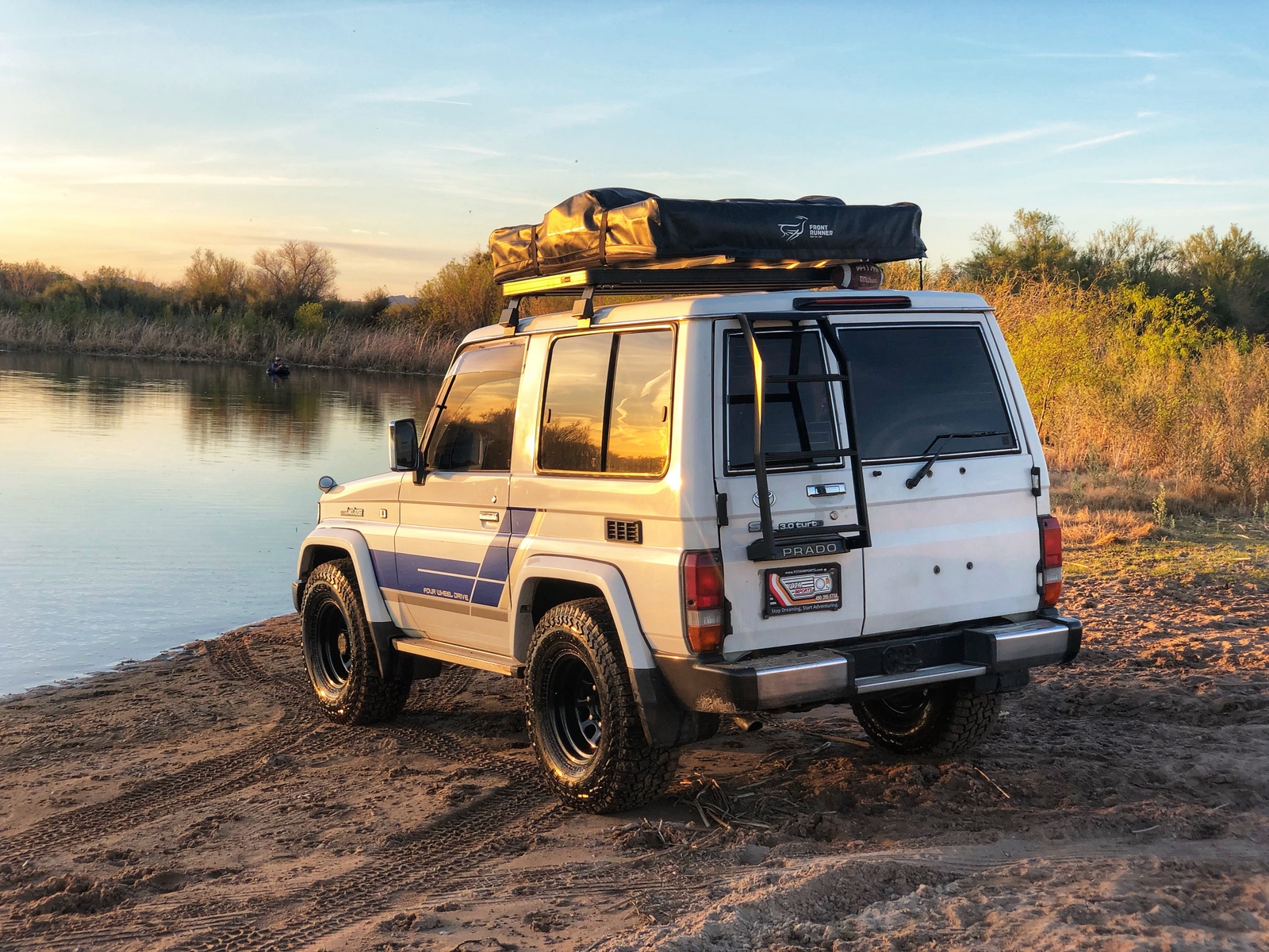 White Prado Land Cruiser with rooftop tent at the riverbank at sunset